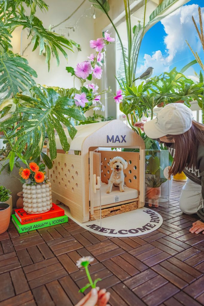 woman-looking-at-dog-in-wooden-kennel-surrounded-by-plants-tmllostiewc